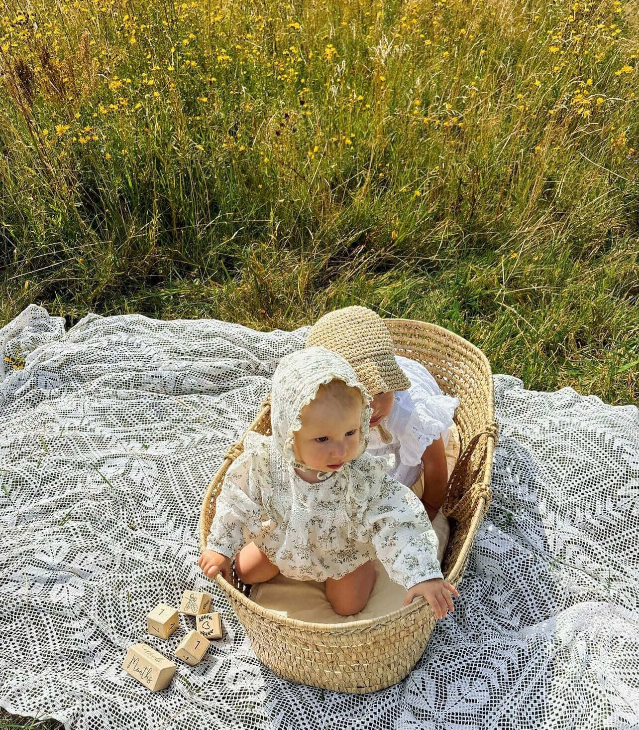 Babies sitting outside in in the long grass in a Clair de Lune Palm Moses basket | Summer Baby Essentials | Parenting & Buying Guides - Clair de Lune UK