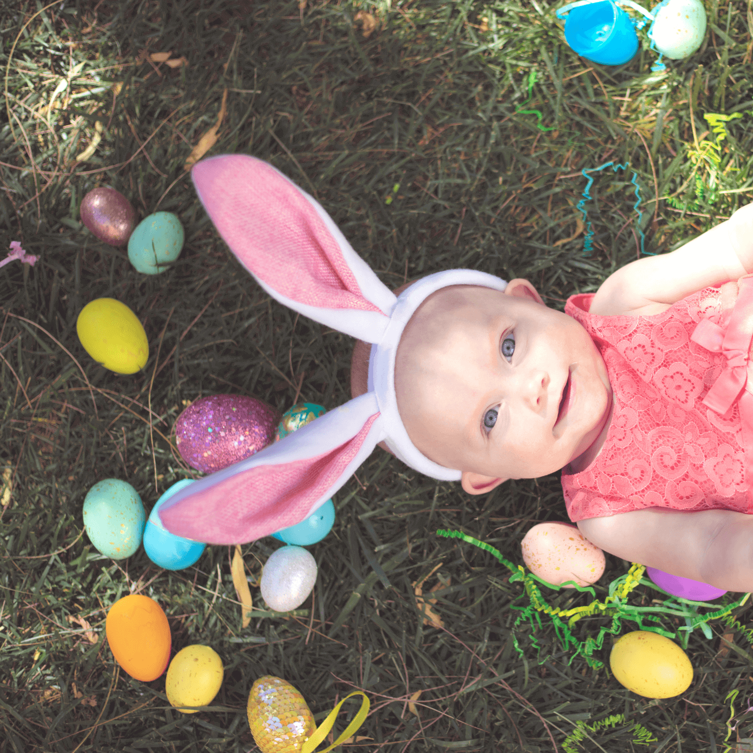 5 Easter Sensory Play Ideas for Your Baby | Toddler girl wearing bunny ears lying on the grass surrounded by plastic, fillable Easter eggs - Clair de Lune UK
