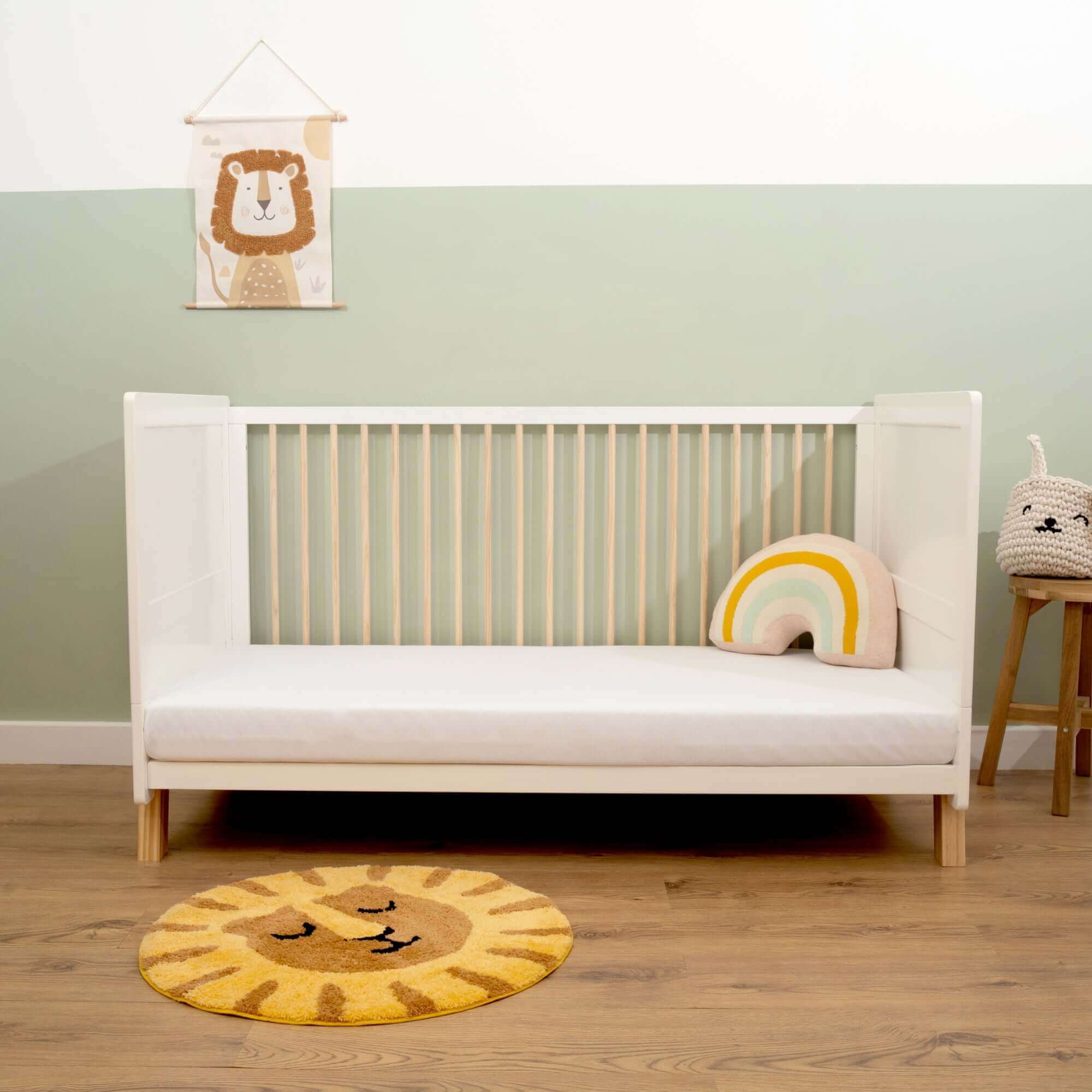Clair de Lune Essentials Cot Bed vs. Oak Cot Bed | Essentials White Cot Bed with a baby rainbow cushion and cot mattress in sage green nursery | Nursery Furniture - Clair de Lune UK