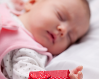 Newborn baby lying asleep on the bed next to a Christmas gift wrapped in red | Family Christmas - Clair de Lune UK