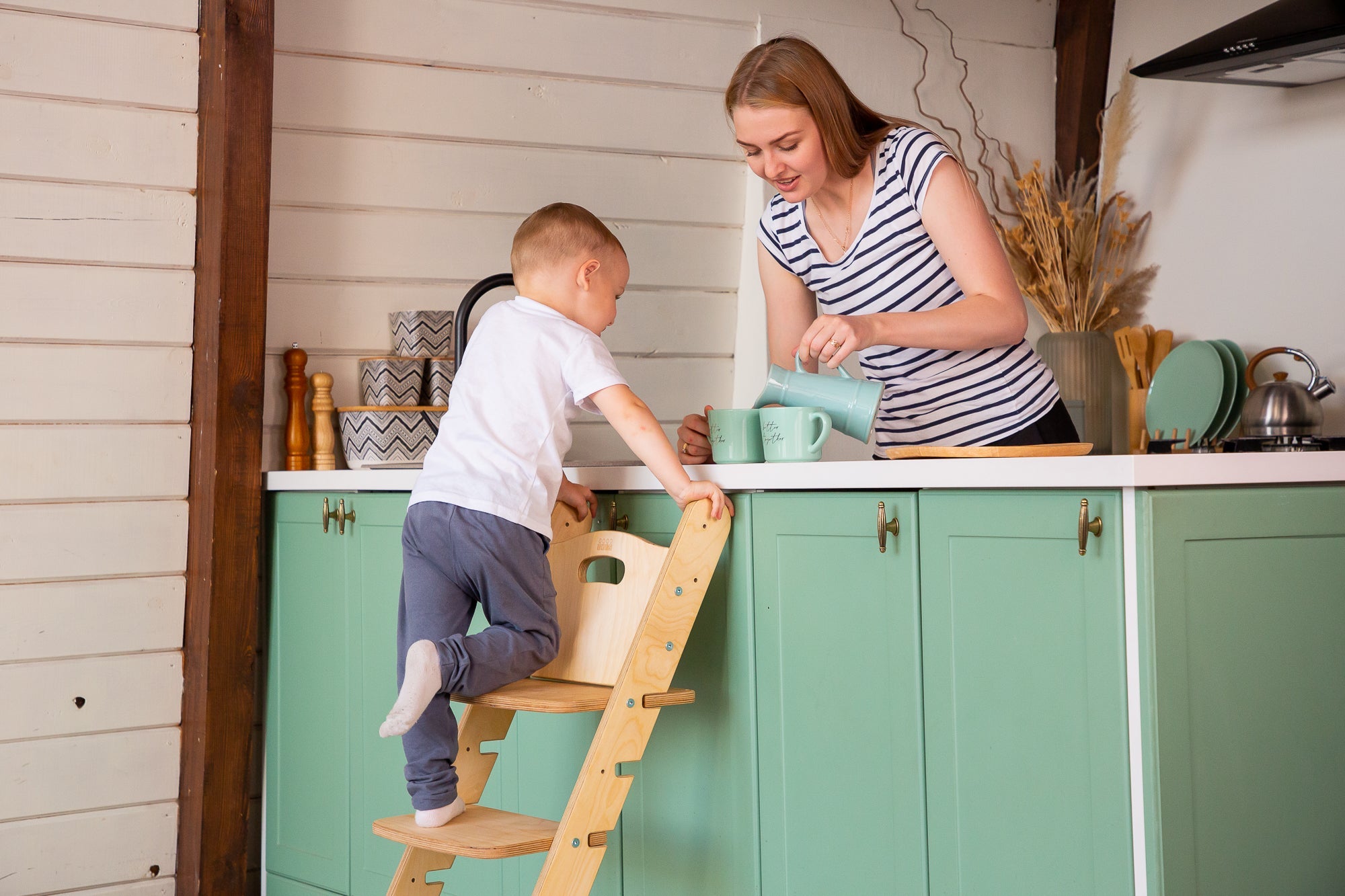Young girl standing on a natural pine kitchen tower in a sage green kitchen | High Chair - Clair de Lune UK