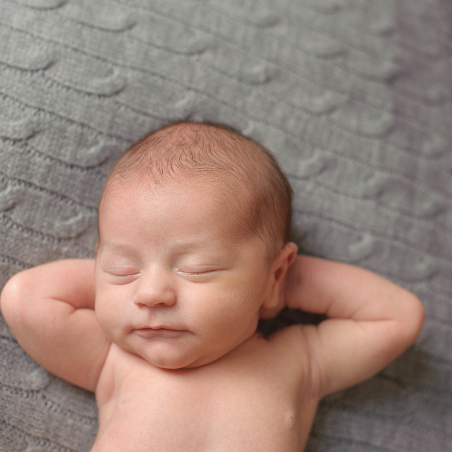 Newborn baby sleeping with arms behind his head on grey blanket - Clair de Lune UK