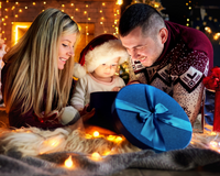Mum, dad and baby wearing a santa hat looking inside a gift box surrounded by twinkling fairy lights | Family Christmas - Clair de Lune UK