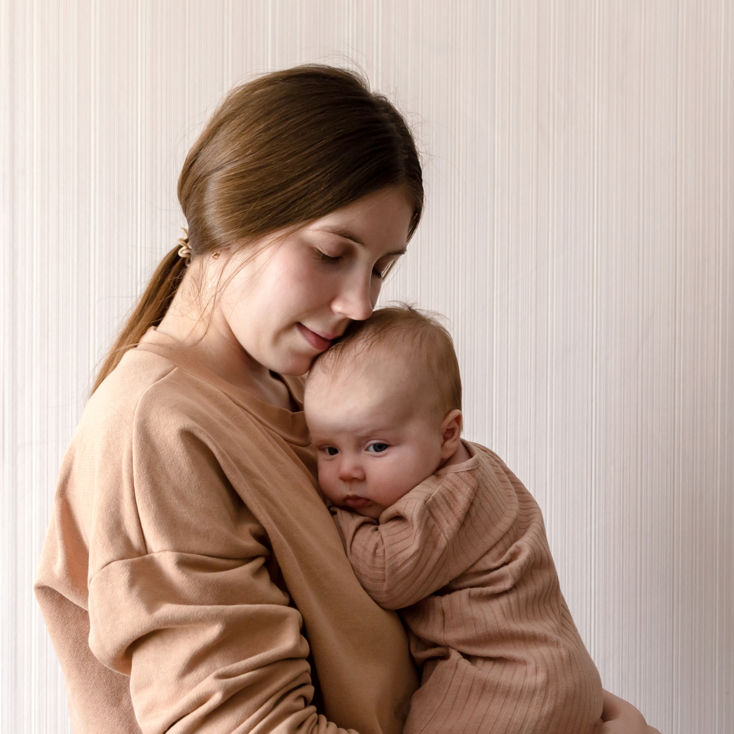 Mum cradling newborn in matching beige outfits - Clair de Lune UK