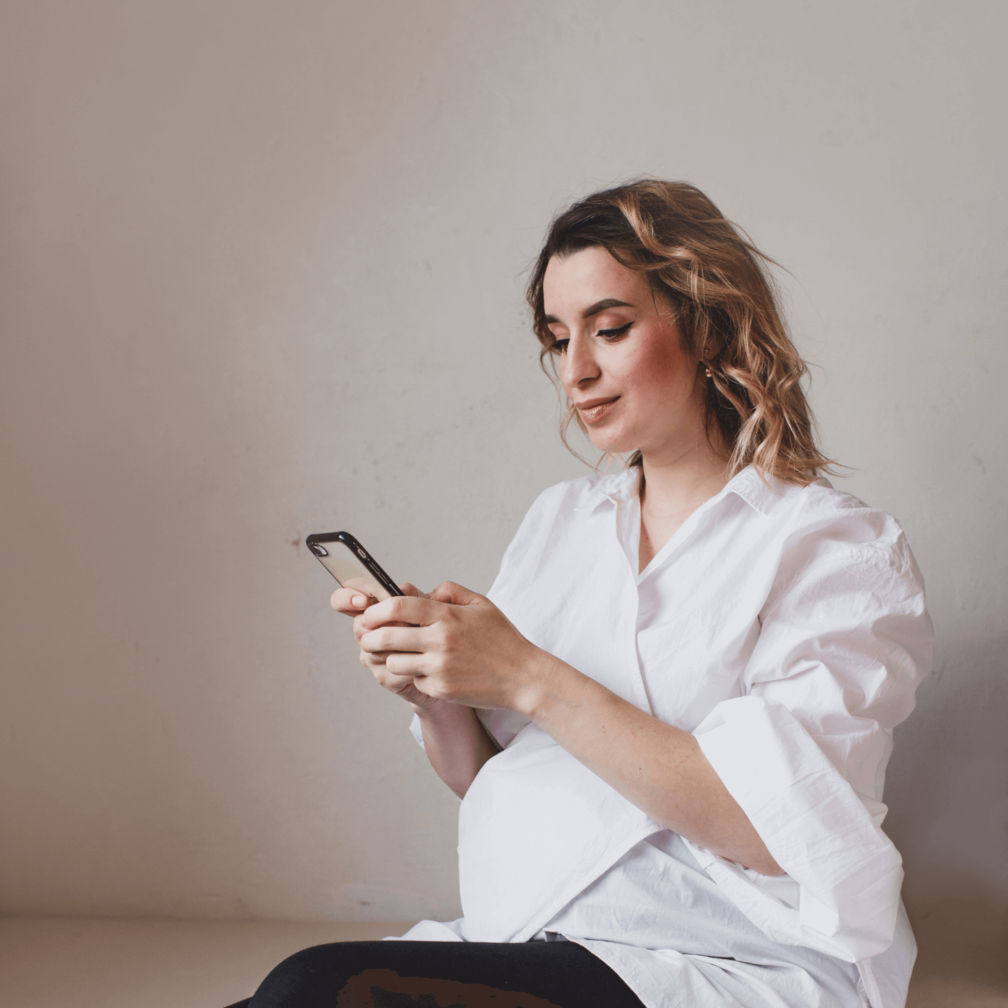 Pregnant mum wearing a white shirt against a grey back drop scrolling on her phone | Pregnancy Tips - Clair de Lune UK