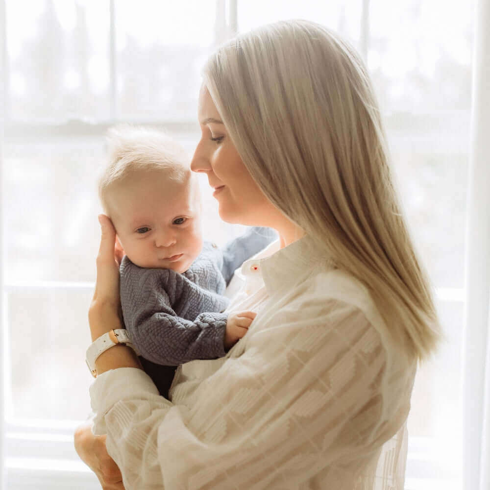 Mum holding her newborn baby boy in front of a light and airy window on Mother's Day | How to Celebrate Mother’s Day as a First-Time Mum - Clair de Lune UK