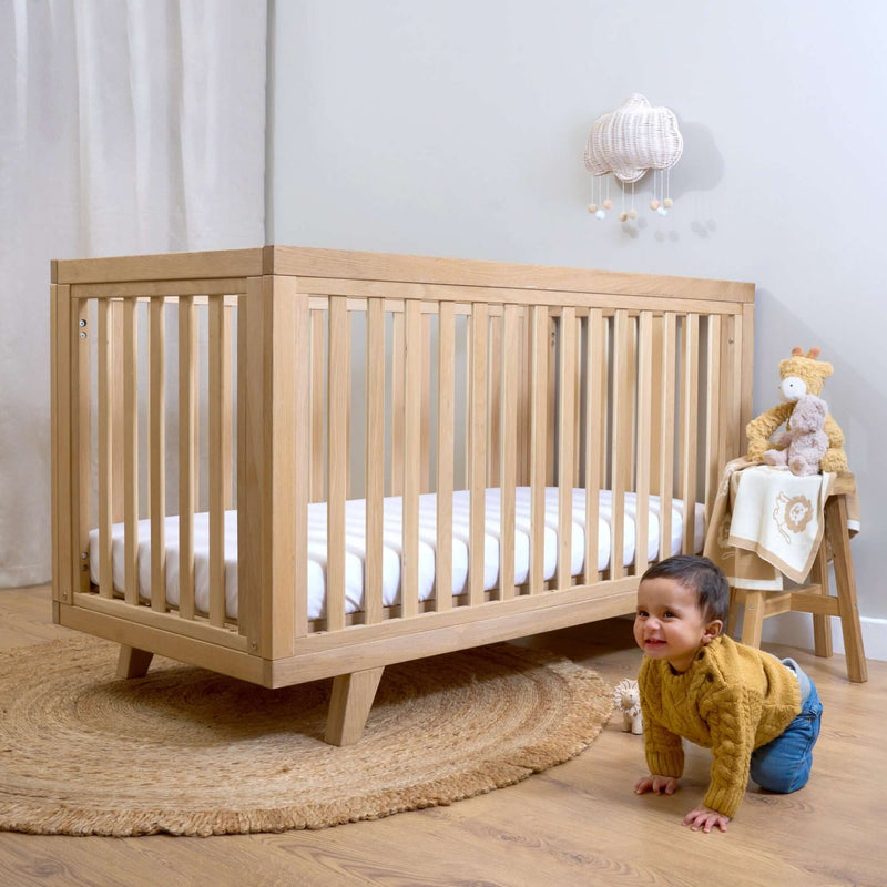 Baby crawling next to the Oak Cot Bed in a Scandi Natural Nursery Room | Cots, Cot Beds, Toddler & Kid Beds | Nursery Furniture - Clair de Lune UK