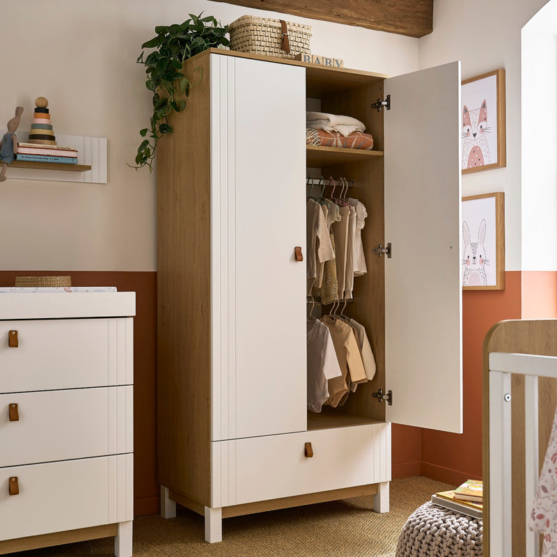 The white and natural double wardrobe of the White and Natural CuddleCo Rafi Nursery Room Sets with baby clothes in a Biritsh countryside cottage nursery room | Nursery Furniture Sets | Room Sets | Nursery Furniture - Clair de Lune UK