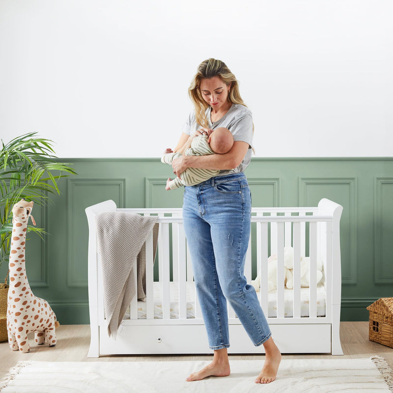 Mum holding her baby in front of the Ickle Bubba Snowdon Classic Cot Bed | Cots, Cot Beds & Toddler Beds | Nursery Furniture - Clair de Lune UK