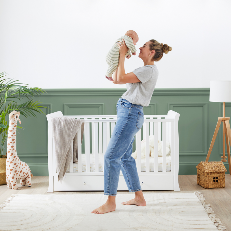 Mum carrying baby in front of the Ickle Bubba Snowdon Classic Cot Bed | Cots, Cot Beds & Toddler Beds | Nursery Furniture - Clair de Lune UK