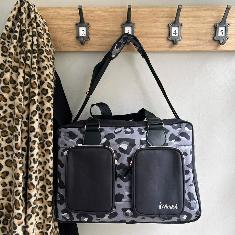 My Babiie Dani Dyer Black Leopard Deluxe Changing Bag hanging on the wall-mounted shelf | Stylish Nappy Bags | Travel With Baby - Clair de Lune UK