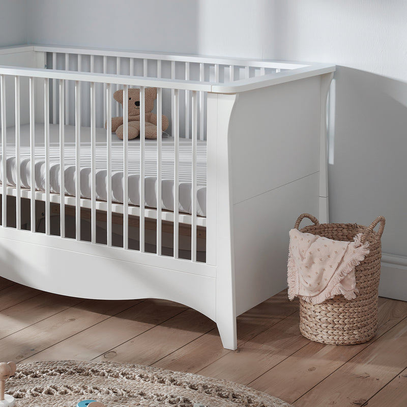 The cot bed of the White CuddleCo Clara 3pc Nursery Set - 3 Drawer Dresser/Changer, Cot Bed & Wardrobe in a natural white gender-neutral nursery | Nursery Furniture Sets | Room Sets | Nursery Furniture - Clair de Lune UK