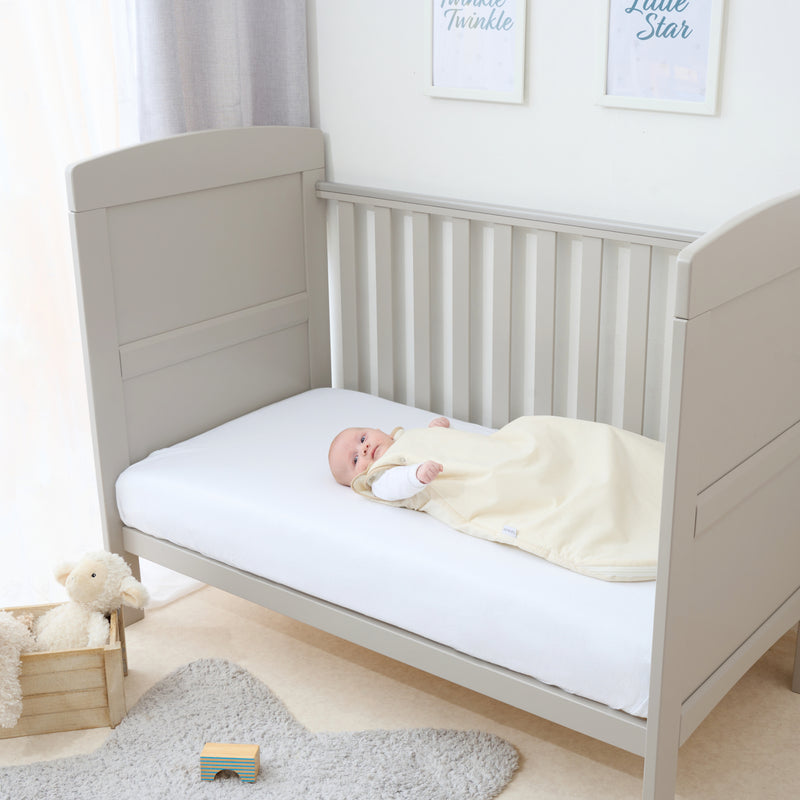 Baby in the Natural Cream Organic Sleeping Bag (0-6 Months) playing in a grey cot bed | Baby Sleep Bags, Shawls, Swaddles & Sleepbags | Nightwear | Nursery - Clair de Lune UK