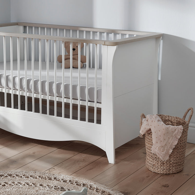 The cot bed of the Ash CuddleCo Clara 3pc Nursery Set - 3 Drawer Dresser/Changer, Cot Bed & Wardrobe in a natural white gender-neutral nursery | Nursery Furniture Sets | Room Sets | Nursery Furniture - Clair de Lune UK