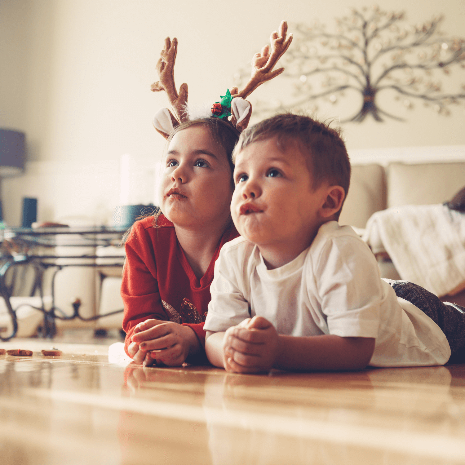 Two children dressed in Christmas jumpers and reindeer antlers lying on the floor watching Christmas films | Family Christmas - Clair de Lune UK