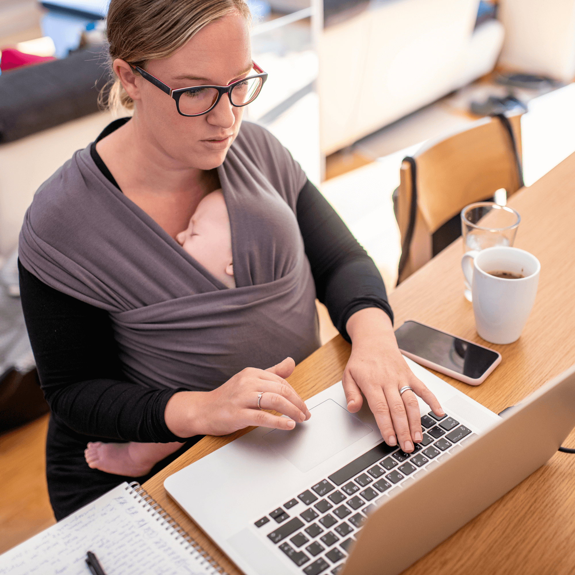 Mum working at her desk with a baby in a sling strapped to her front | Working from home with children - Clair de Lune UK