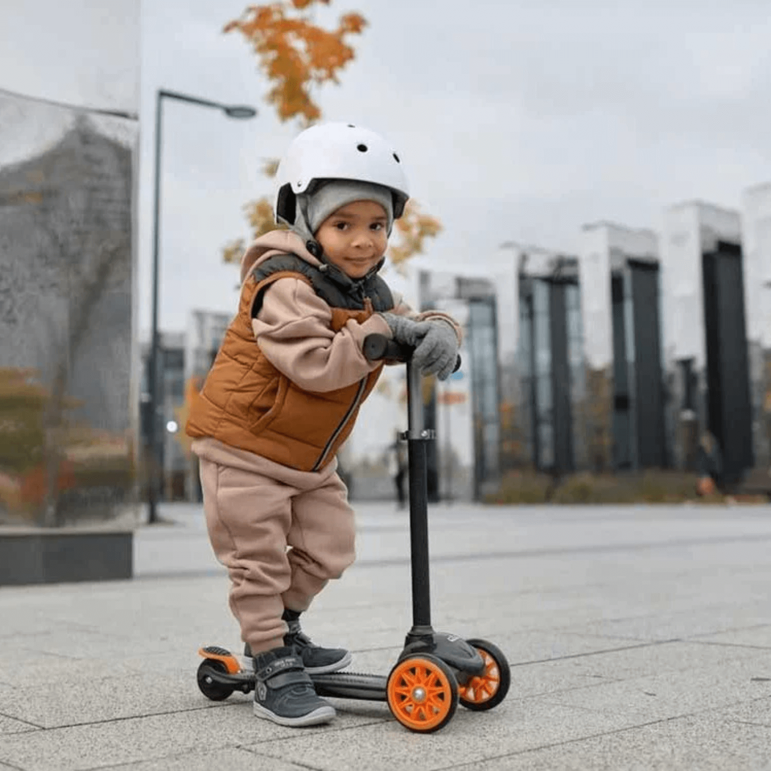 Toddler boy wearing safety helmet riding scooter in an urban city centre | Outdoor childrens toys - Clair de Lune UK