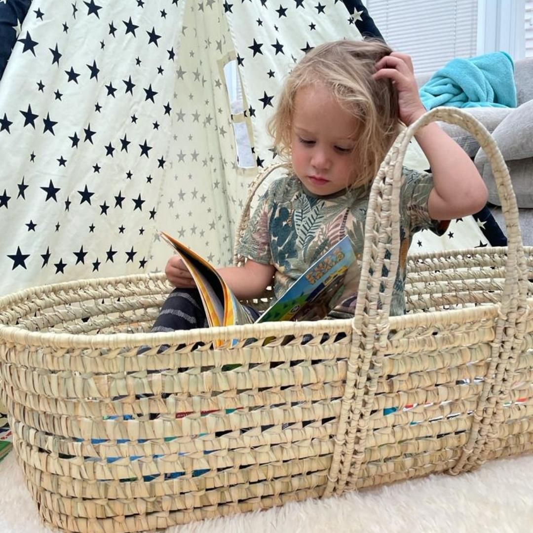 Toddler sat reading in an undressed Palm moses basket in front of a tee-pee | Upcycling baby products - Clair de Lune UK