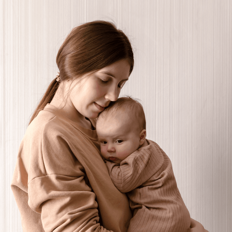 5 Ways to Celebrate Baby's First Valentines Day | Mum cradling newborn in matching beige outfits - Clair de Lune UK