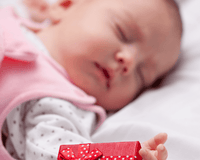 Newborn baby lying asleep on the bed next to a Christmas gift wrapped in red | Family Christmas - Clair de Lune UK