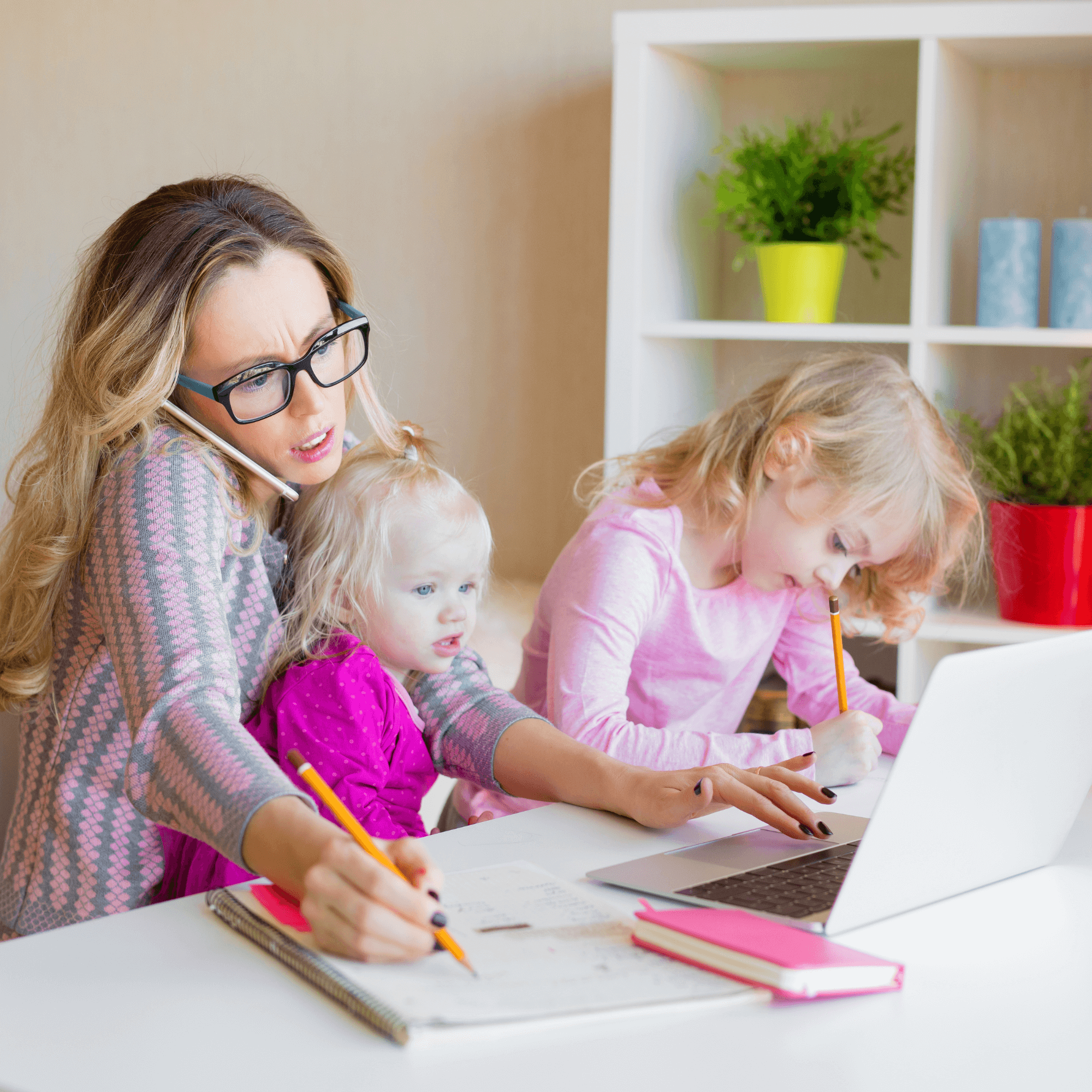 Mum wearing glasses holding her two children while on the phone and working on her laptop | Work/Life balance - Clair de Lune UK