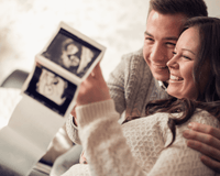 Dad and pregnant mum sat on the sofa with their scan photo | Black Friday - Clair de Lune UK