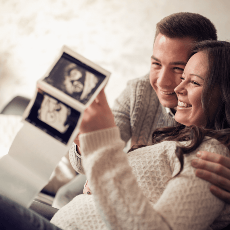 Dad and pregnant mum sat on the sofa with their scan photo | Black Friday - Clair de Lune UK