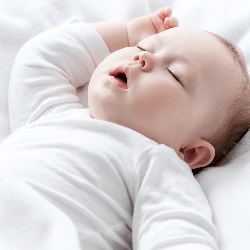 Baby lying fast asleep in the cot on a white cotton cot bed fitted sheet | Parenting tips & advice - Clair de Lune UK