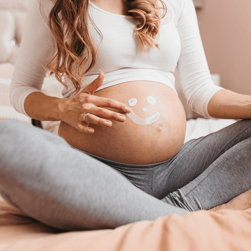 Pregnant mum sat cross legged on the floow holding her baby bump | Parenting tips and advice - Clair de Lune UK