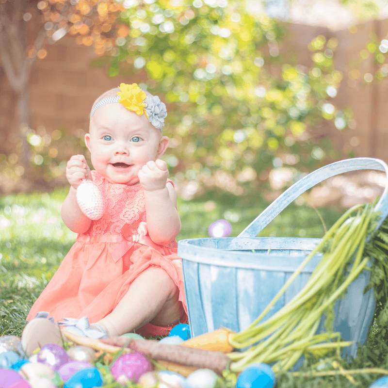 Baby wearing a flower headband sat on the grass next to an easter basket holding a plastic easter egg | Easter Activities | Family Time - Clair de Lune UK