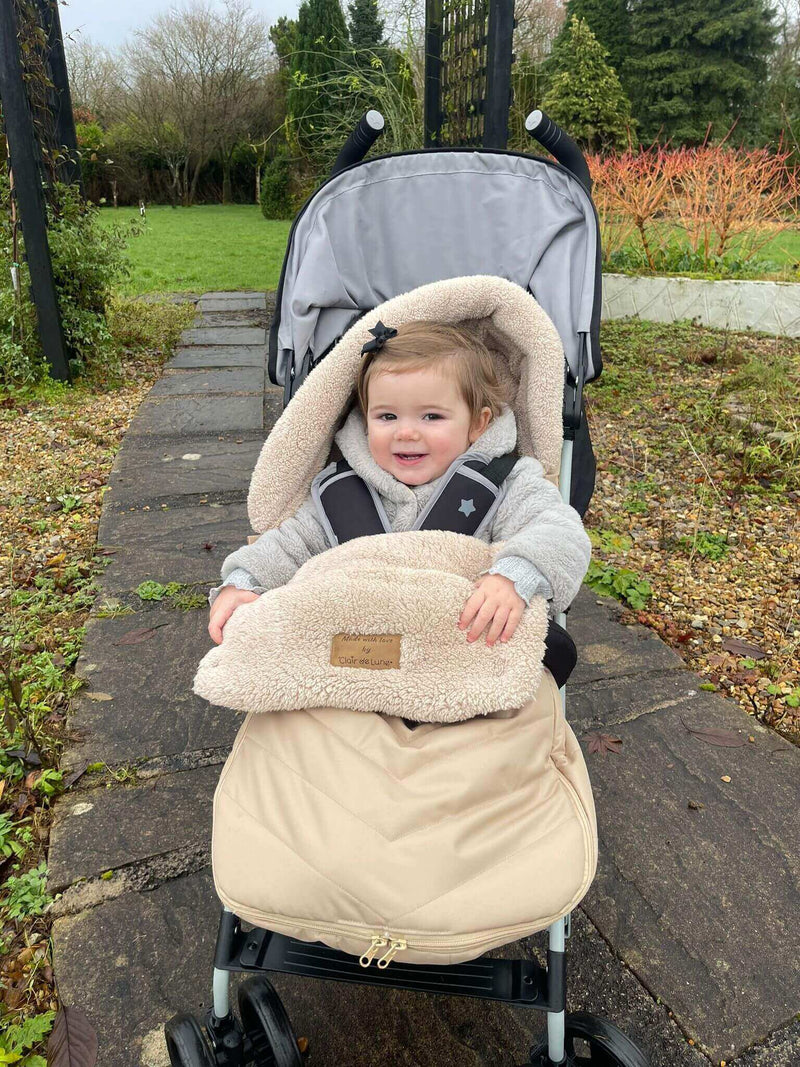 Top 5 Winter Warmers for Your Baby | Baby girl in Beige Snug footmuff enjoying a stroll in the park | Pushchair Accessories - Clair de Lune UK