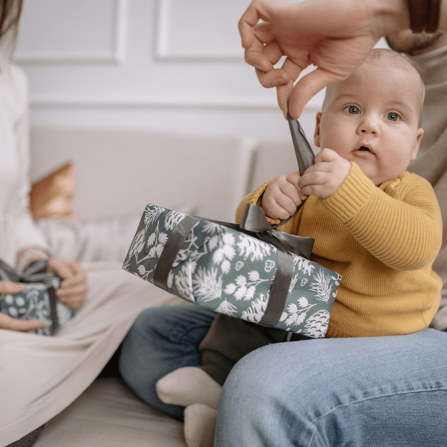 Baby say on mums knee on the floor opening a Christmas present | Family Christmas - Clair de Lune UK