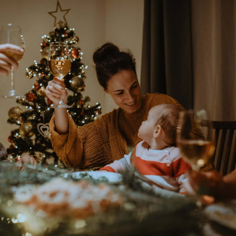 Family having a cheers at Christmas dinner with baby on her lap | Baby's First Christmas - Clair de Lune UK