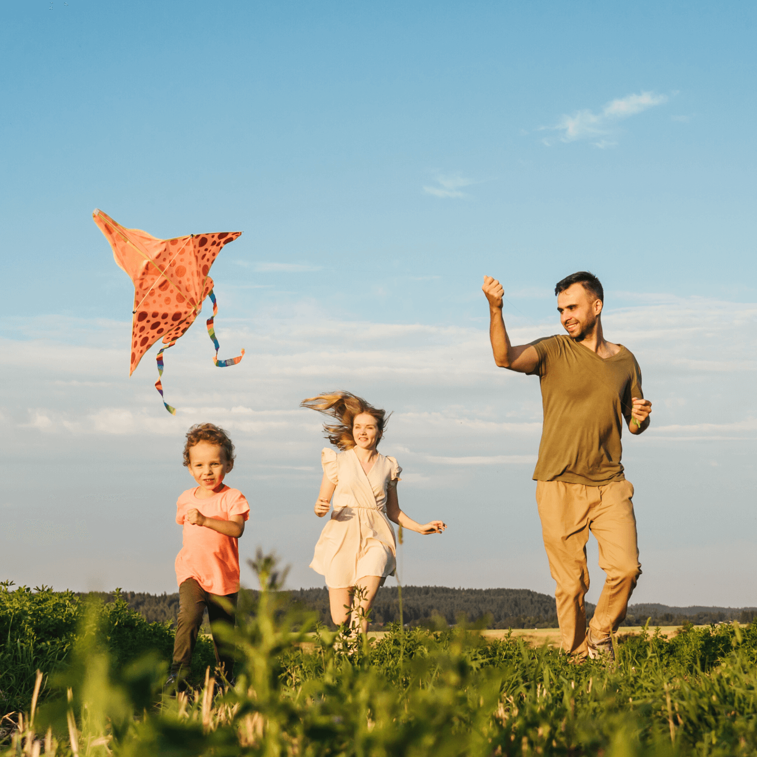 Dad and two kids on top of a grassy hill flying a kite together and smiling on a sunny day | News - Clair de Lune UK