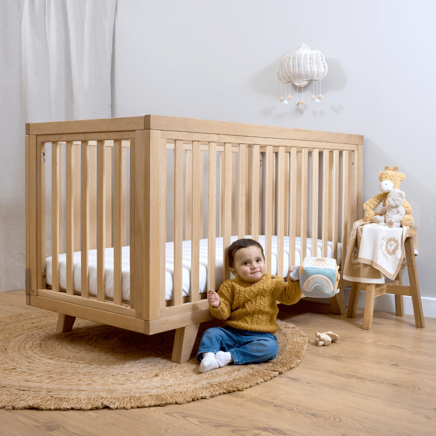 Toddler playing next to the Oak Cot Bed in a beautiful neutral nursery | Nursery Furniture - Clair de Lune UK