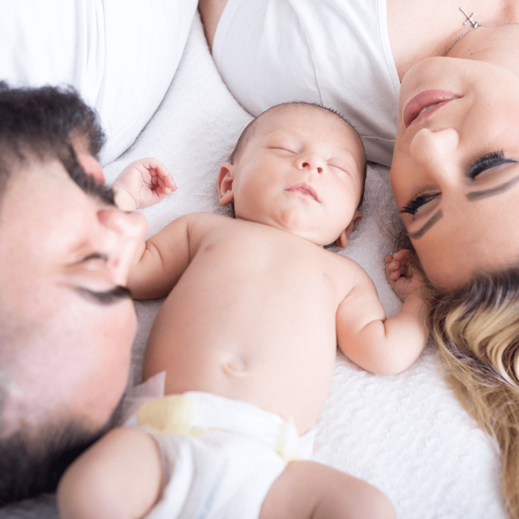 Mum and dad lying on the bed with their newborn baby | Parenting tips and advice - Clair de Lune UK