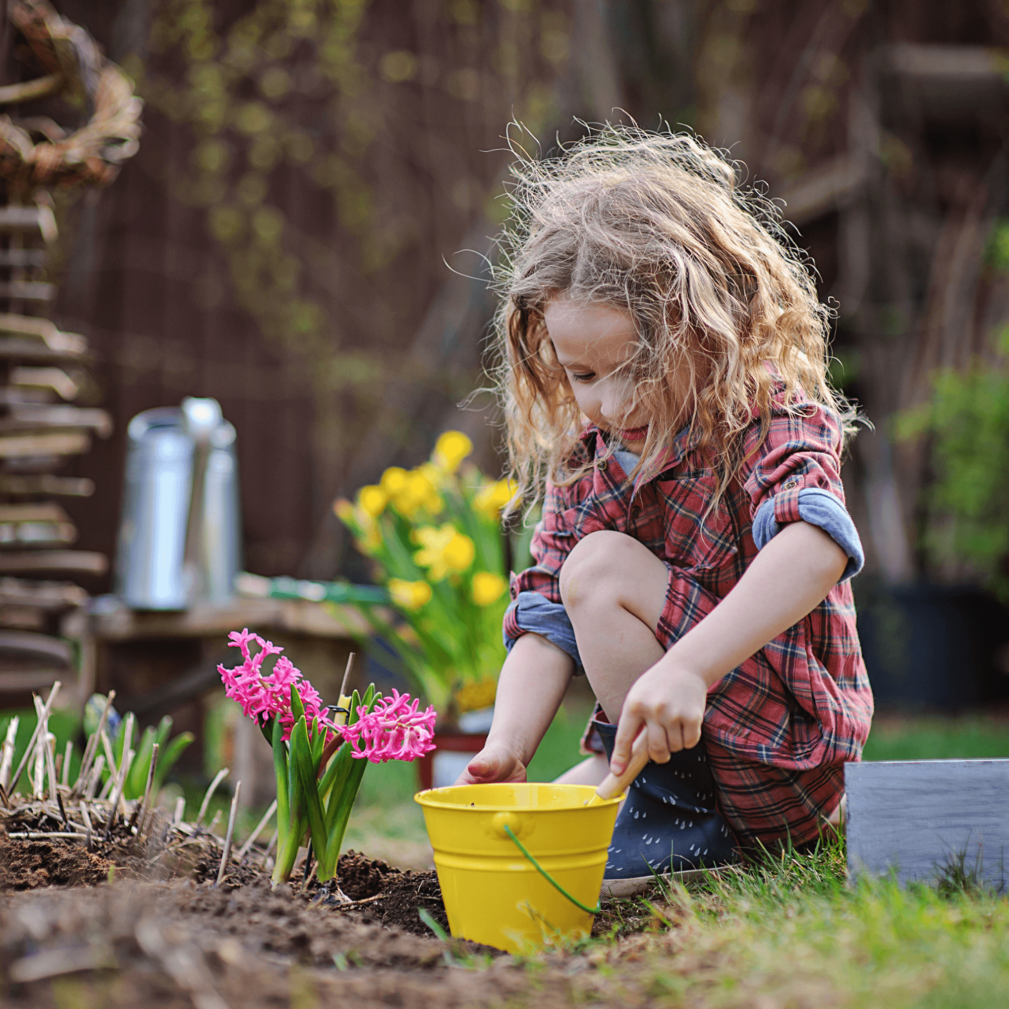 Toddler with curly blonde hair kneeling in the garden planting flowers in a yellow pot | Family Time | Summer Fun - Clair de Lune UK