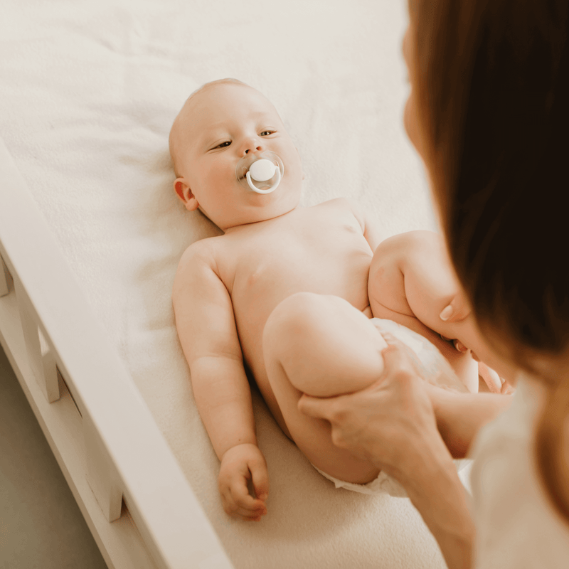 Toddler lying on a hospital bed sucking a dummy while the doctor moves their legs around to check for hip dysplasia - Clair de Lune UK