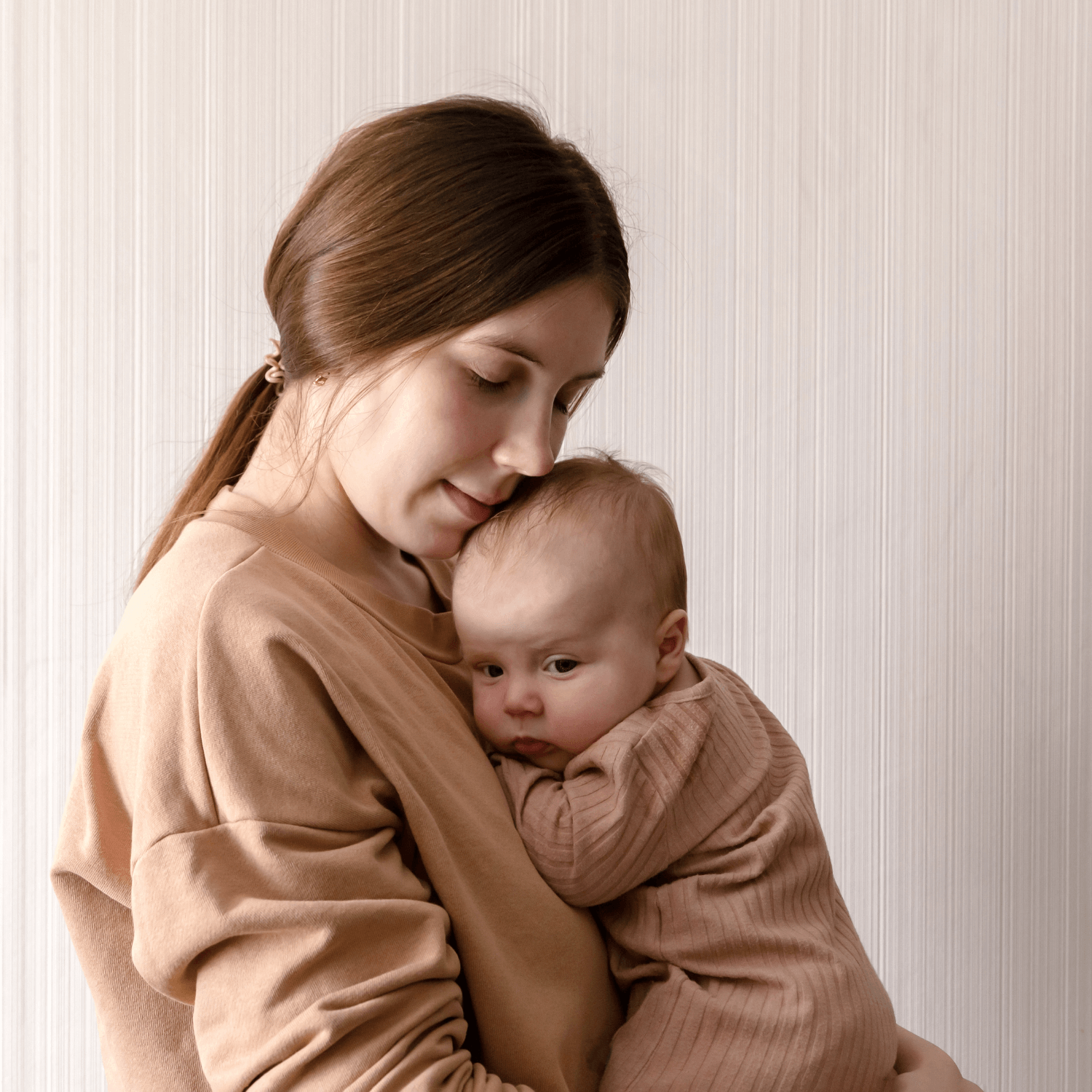 Mum cradling newborn in matching beige outfits - Clair de Lune UK