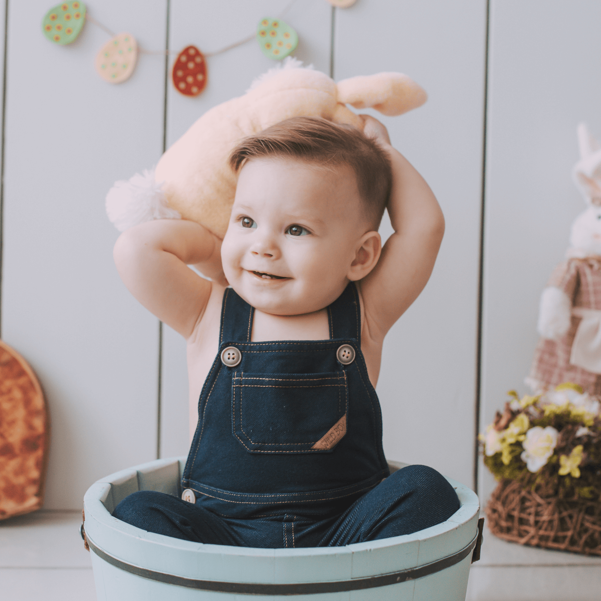 Baby boy wearing dungarees and holding a rabbit soft toy over his head | Easter Celebrations | Family Time - Clair de Lune UK