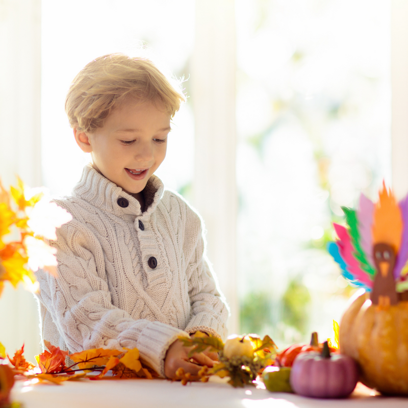 Young boy dressed in a warm cream jumper making Autum crafts from leaves and pumpkins | Toddler Crafts - Clair de Lune UK