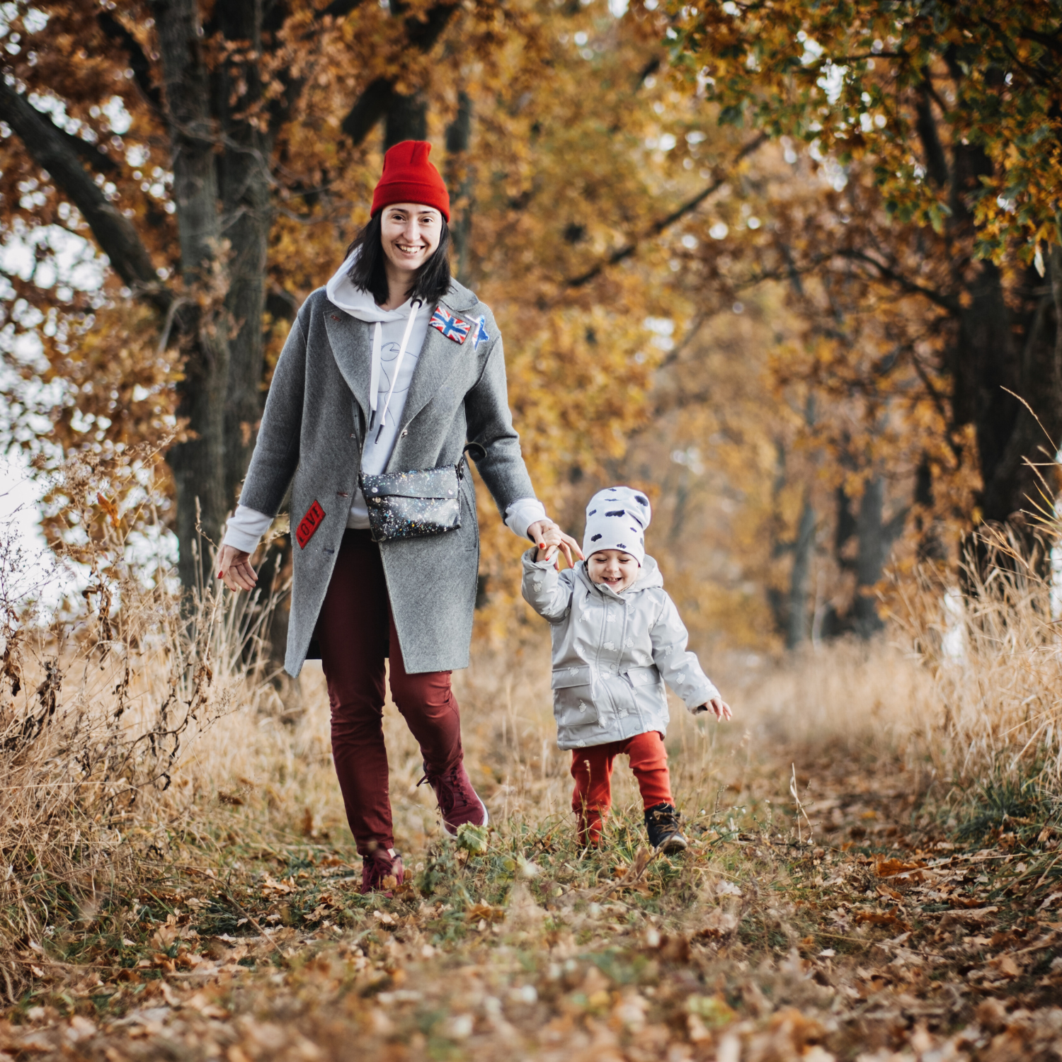 Mum and toddler girl wrapped up in coats and hats holding hands, walking down a path with autumn leaves and trees | News - Clair de Lune UK