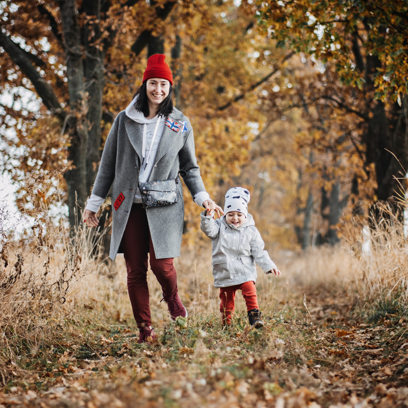 Mum and toddler girl wrapped up in coats and hats holding hands, walking down a path with autumn leaves and trees | News - Clair de Lune UK