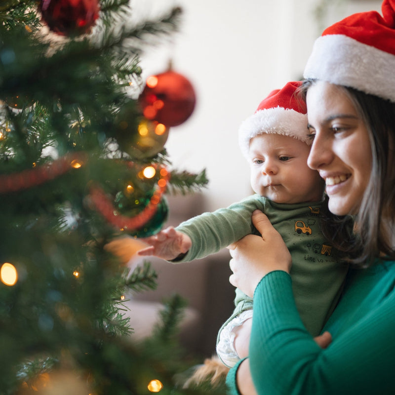 Mum holding newborn baby and showing them the christmas tree while wearing santa hats | Baby's First Christmas | Family Time - Clair de Lune UK