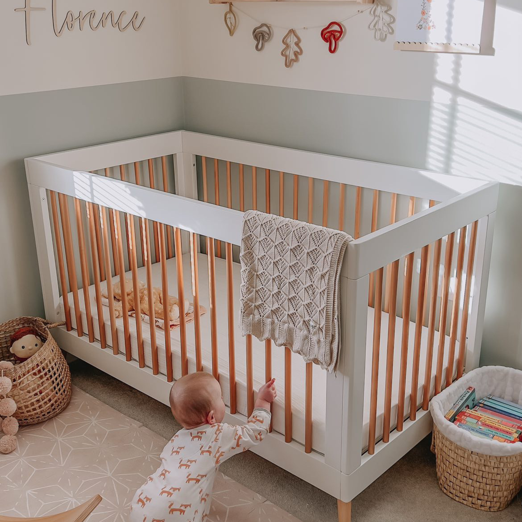 White and oak cot in a sage and white nursery with a toddler crawling and pulling themselves towards in | Cots and Cot Beds | Nursery Furniture - Clair de Lune UK