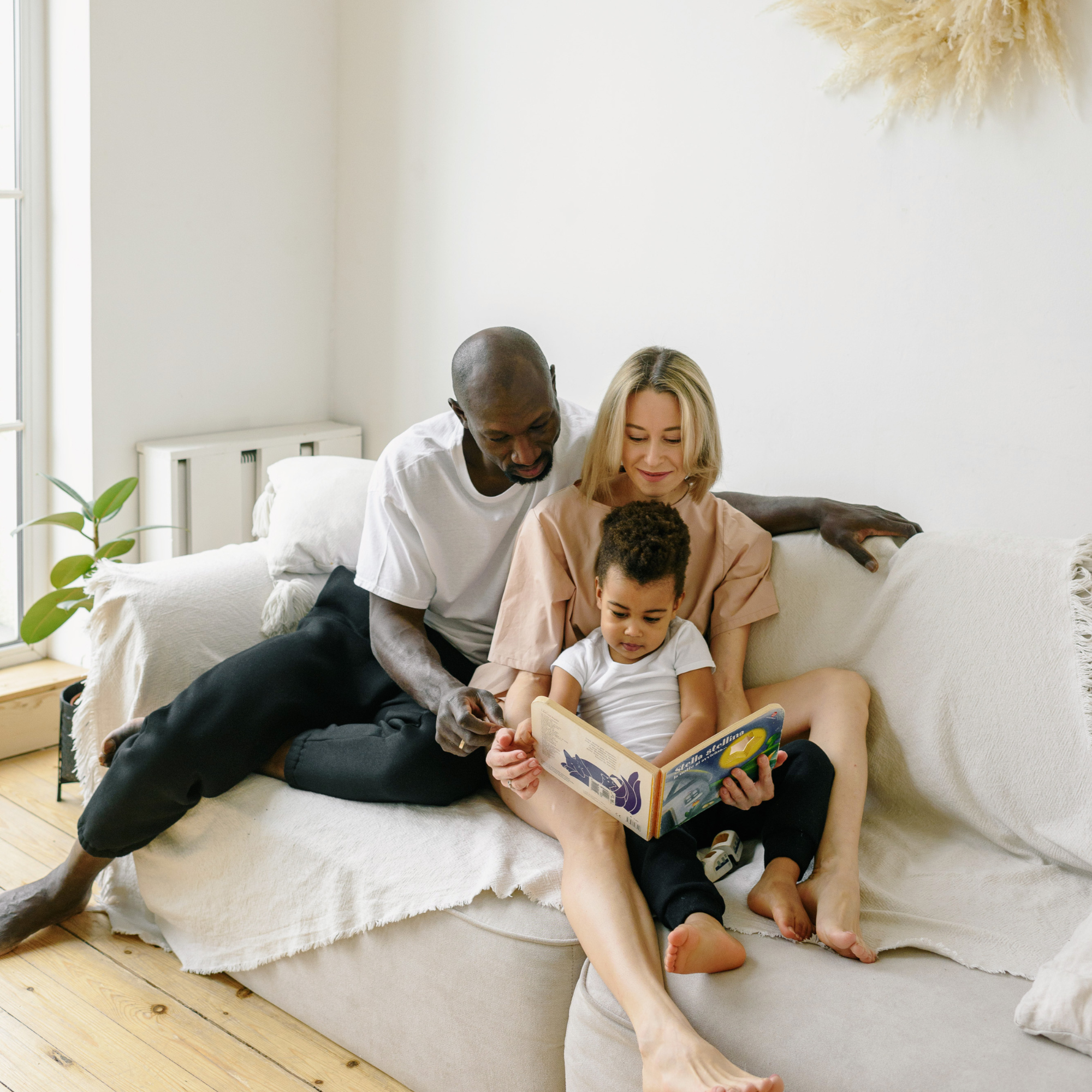 Mum, dad and toddler lying on the sofa reading a children's book | Family time - Clair de Lune UK