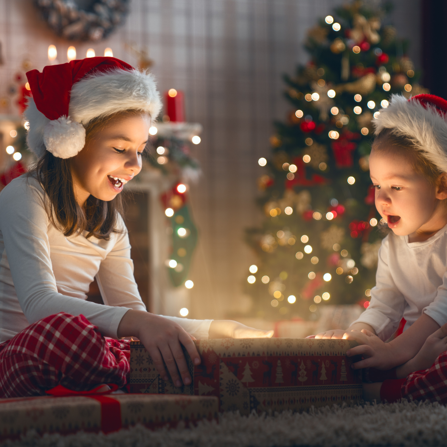 Two children sat in front of the Christmas tree in the dark and opening a gift | Family Christmas - Clair de Lune UK