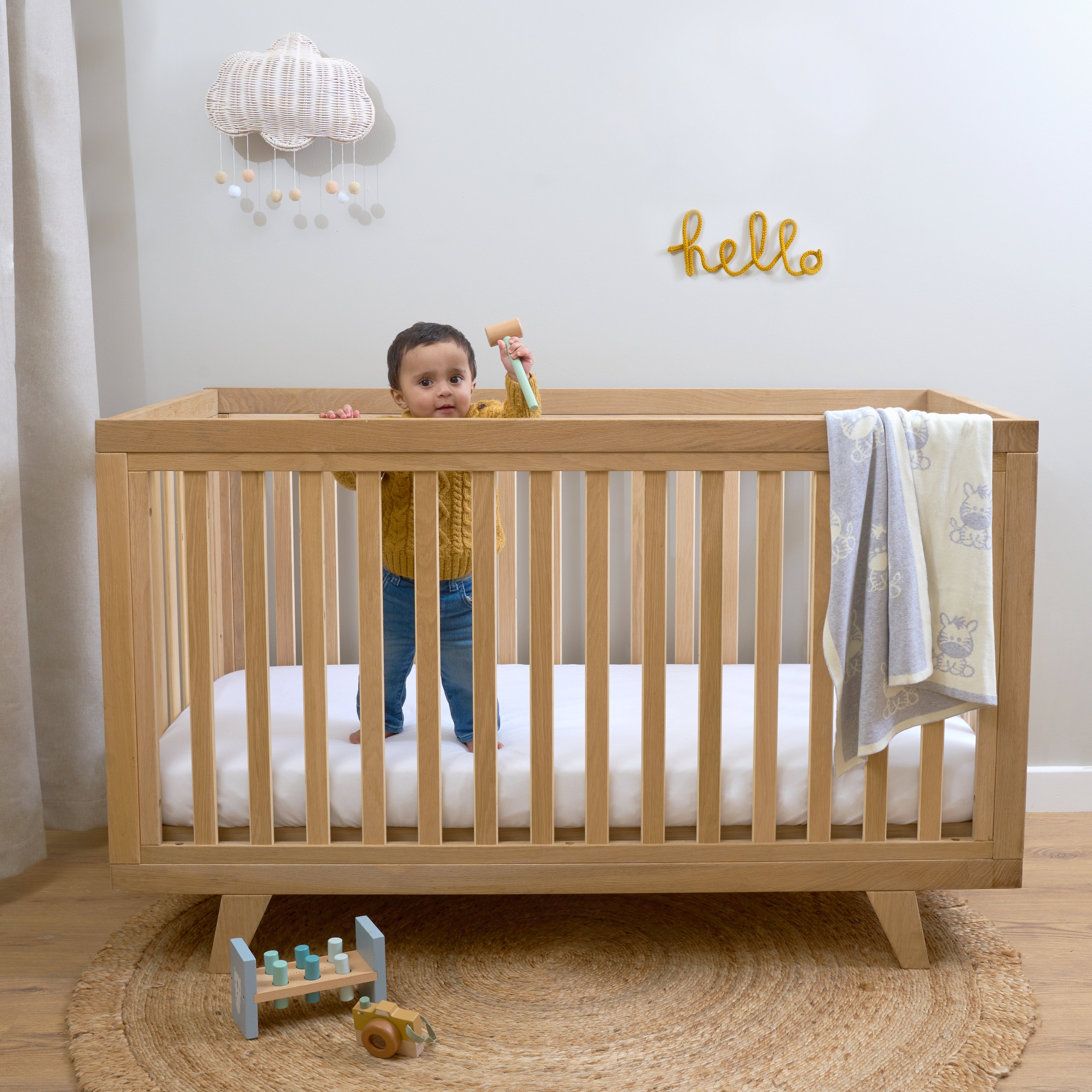 Toddler boy standing in the Natural Oak Cot Bed in baby room | Nursery Furniture - Clair de Lune UK