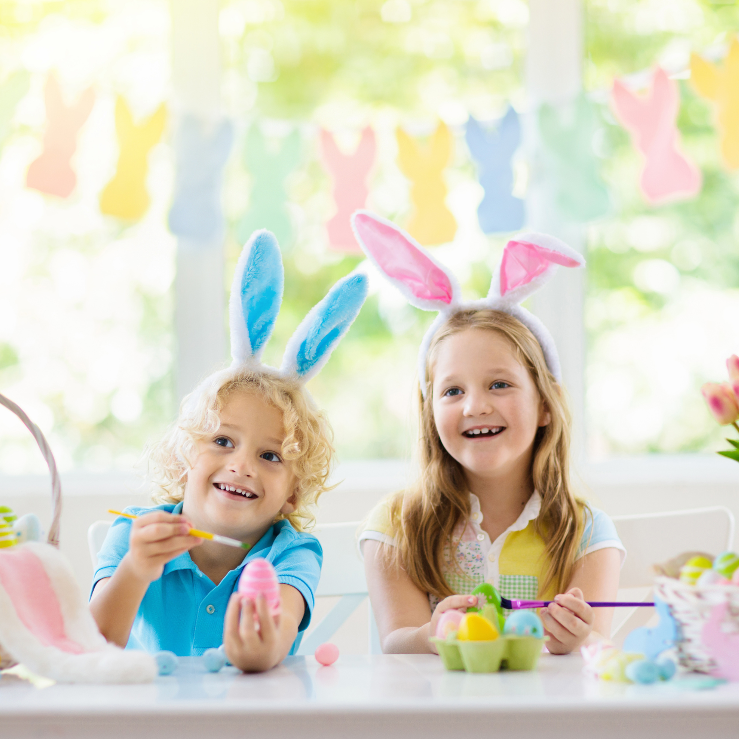 Toddlers wearing bunny ears painting easter eggs surrounded by bunny bunting - Clair de Lune UK