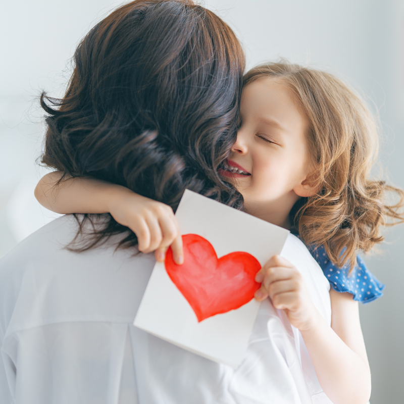 Girl hugging mum tightly while holding DIY heart card | Mother's Day - Clair de Lune UK